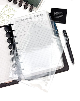 Discbound planner pocket sleeves with quarterly planning insert, pen, and card on a white surface