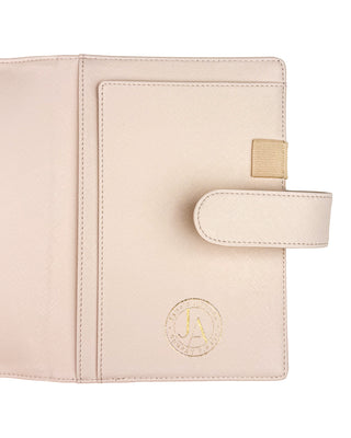 Close-up of the inside right panel of a light beige planner cover with a textured finish. Features include a full-length slip pocket, an elastic pen loop, a secure magnetic snap closure strap, and a gold foil Jane’s Agenda logo embossed in the lower corner.