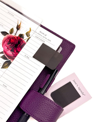 Featuring Black P.E.T. page flags marking a page in a purple wrap around vegan leather planner, with the vibrant roses hybrid dashboard on a white background. 
