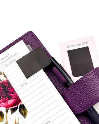 Featuring Black P.E.T. page flags marking a page in a purple wrap around vegan leather planner, with the vibrant roses hybrid dashboard on a white background. 