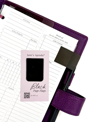 Featuring Black P.E.T. page flags marking a page in a purple wrap around vegan leather planner on a white background. 
