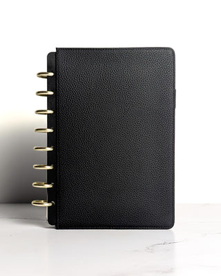 Standing view of closed planner with a black snap on cover from Jane's Agenda and gold discs visible on the spine