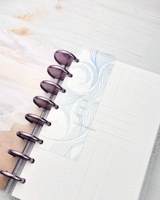 Purple binding sdiscs on a discbound planner with a blu mbre swirl plastic page finder in front of an insert page.