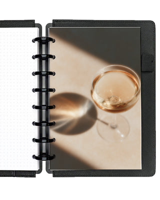 A glass of champagne disc bound planner dashboards, snapped into a planner with Black Plastic Discs and Black Vegan Leather Snap-on Cover on a white background. 