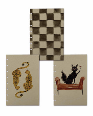 Three artistic discbound planner covers displayed together, featuring unique hand-painted designs: a soft brown watercolor checkerboard pattern, two spotted cheetahs facing each other, and a whimsical black cat sitting on a bench while holding a martini glass.