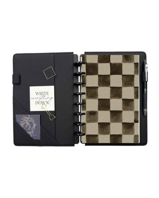 Open black pebbled planner cover with interior storage pockets, elastic pen loop, magnetic bookmark, and decorative cards. A removable checkerboard dashboard is displayed on black discs, with a pen secured in the built-in pen loop.