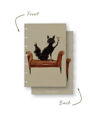 Front and back views of a removable discbound planner dashboard featuring a whimsical illustration of a black cat sitting on a vintage bench while holding a martini glass. The front showcases the playful artwork, while the back features a coordinating neutral beige design.