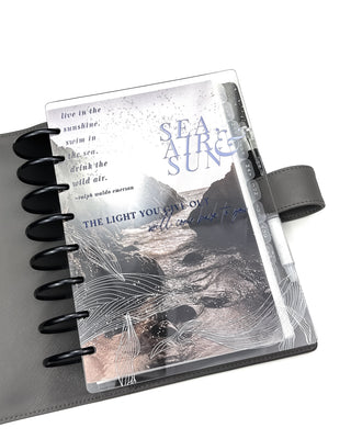 Jane's Agenda gray discbound planner vegan leather cover with coastal ocean "Sea Air & Sun" embossed clear plastic snap on cover, whale illustration, and inspirational affirmation over moody beach aesthetic planner cardstock dashboard