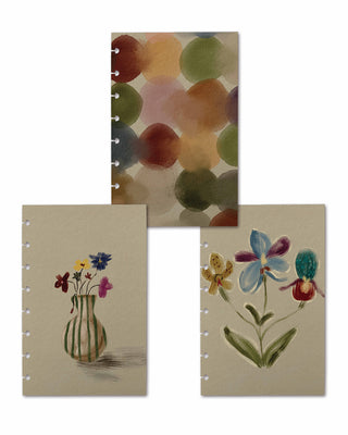 Three removable discbound planner dashboards displayed together, each featuring a unique artistic design. The collection includes an abstract watercolor pattern of overlapping multicolored circles, a striped green vase holding delicate wildflowers, and a whimsical floral illustration with oversized blue, purple, yellow, and teal blooms on a soft cream background.