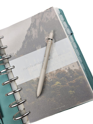 Beige Pilot erasable Frixion pen on a discbound planner with scenic cover over a white background