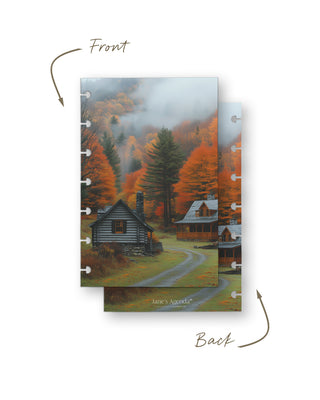 Front and back views of a discbound planner dashboard featuring rustic log cabins nestled among vibrant orange autumn trees in a misty forest landscape.