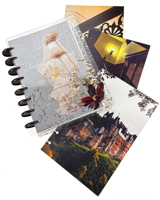 Open Jane’s Agenda discbound planner with dark metallic discs, featuring layered clear dashboards with handwritten script and delicate pressed flowers in cream, gold, and burgundy tones, displayed alongside coordinating staircase, interior, and castle dashboards.