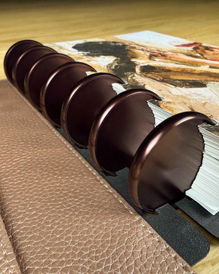 Jane's Agenda discbound planner macro detail shot showing 2" glossy chocolate metal discs on rose gold pebbled faux leather cover with stacked planner pages