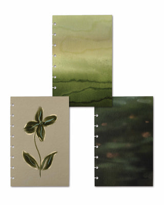 Three coordinating discbound planner covers displayed together, each featuring a nature-inspired design. The collection includes a vintage botanical flower illustration, a soft green watercolor landscape, and a dark moody abstract landscape, offering complementary styles for customizable planners.