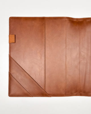 Interior view of a warm brown leather planner cover displayed open against a white background. The left side features two diagonal slip pockets and a coordinating elastic pen loop, while the smooth leather interior showcases clean stitching and a spacious design for organizing planner essentials.