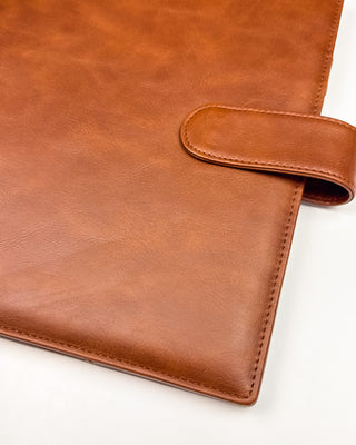 Close-up of a warm brown leather planner cover highlighting the smooth leather exterior, rounded corner, and matching snap closure. Fine stitching and the natural leather grain are showcased against a clean white background, emphasizing the cover’s classic craftsmanship.