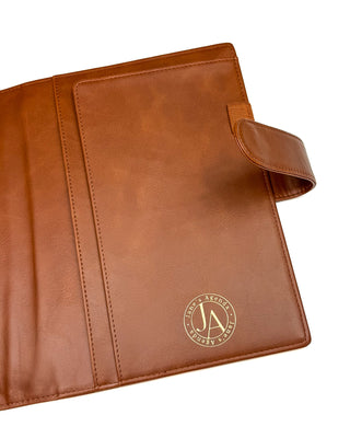 Interior view of a warm brown leather planner cover displayed open against a white background. The cover features smooth leather slip pockets, a coordinating elastic pen loop, a secure snap closure, and a gold foil Jane’s Agenda logo, combining elegant organization with timeless style.