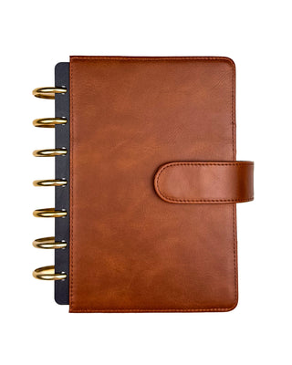 Front view of a warm brown leather planner cover with a secure snap closure, paired with gold metal disc rings and black planner dividers peeking from the left side. Displayed against a clean white background, the cover features a smooth, timeless finish with a classic, minimalist design.