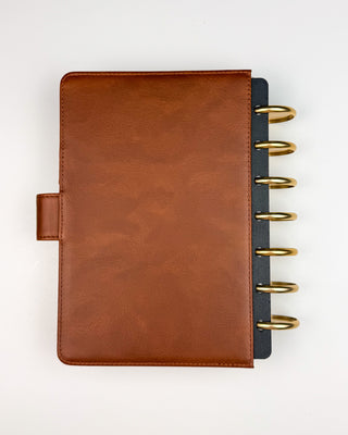 Back view of a warm brown leather planner cover with a smooth, classic finish, paired with gold metal disc rings and black planner dividers visible along the right edge. Displayed against a white background, the minimalist design highlights the rich leather texture and timeless craftsmanship.