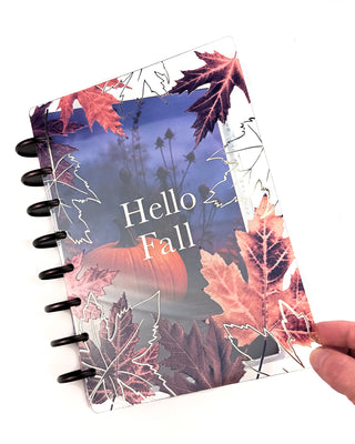 Jane’s Agenda discbound planner with dark metallic discs, featuring a clear fall leaf cover with “Hello Fall” in white lettering layered over a moody pumpkin dashboard in blue and purple tones.