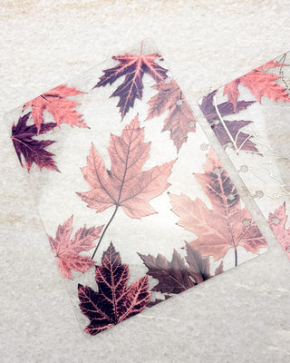 Clear discbound planner cover featuring scattered maple leaves in soft pink, burgundy, and mauve tones, with a matching leaf-patterned piece partially visible beside it.