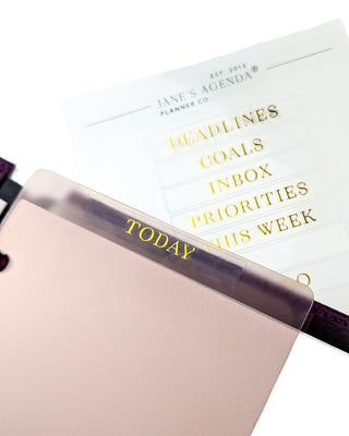 hybrid planner dashboard with a clear adhesive gold foiled hybrid label on it and other gold foil adhesive labels in the background