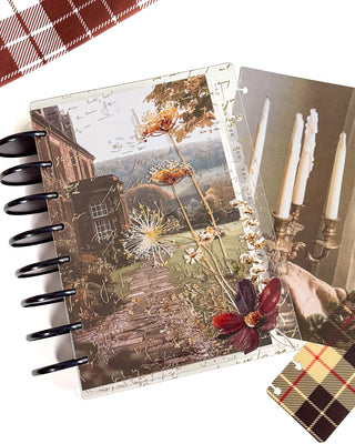 A disc-bound planner with a vintage-style floral cover with an underlying dashboard featuring a cottage scene, flowers, and candles, shown alongside a matching plaid bookmark on a white background.