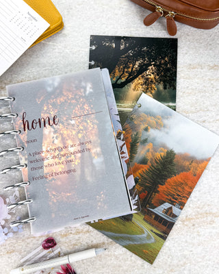 Jane’s Agenda fall planner collection featuring a translucent “home” definition vellum dashboard layered over warm autumn foliage, paired with scenic dashboards of a misty forest cabin and sunlit trees. Styled with silver discs, a white pen, and warm mustard and brown accessories.