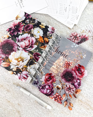 Jane’s Agenda fall-themed discbound planner featuring a translucent “home” definition dashboard layered with burgundy, plum, and red florals, berries, and autumn foliage. Paired with a coordinating floral cover featuring oversized cream, pink, and burgundy blooms on a dark background, silver discs, and a white pen.