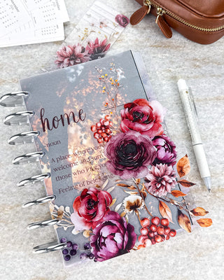 Jane’s Agenda fall-themed discbound planner featuring a translucent “home” definition vellum dashboard layered with rich burgundy, plum, and red floral accents, berries, and warm autumn foliage. Styled with silver discs, a white pen, and coordinating floral accessories.