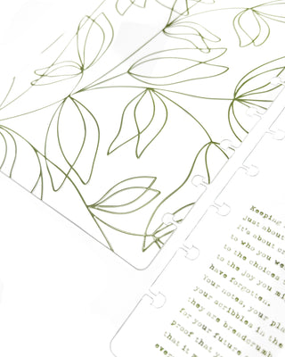 Green floral design on a clear plastic discbound planner cover with a quote in green text lying on a white background.