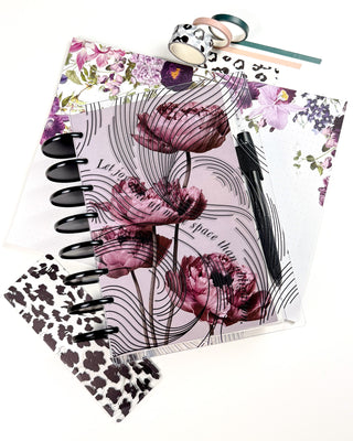 planner cover featuring deep mauve and burgundy floral artwork with flowing black ink line patterns over a soft blush background. The disc bound planner is styled with black discs, floral planner inserts, black-and-white animal print accessories, coordinating washi tape, and a black pen on a white background.