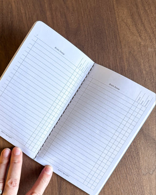 Open notebook with grid and lined pages on a wooden surface, held by a hand.