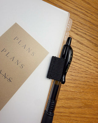 Frosted discbound planner dashboard with an elastic pen loop on a dark background. 