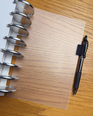 Frosted discbound planner dashboard with an elastic pen loop attached to a discbound planner on a dark background. 