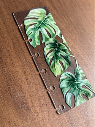 A one size fits all clear plastic page finder for discbound planners featuring green monstera leaves.