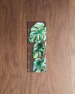 clear plastic discbound planner page finder with monstera leaves on a dark wooden background.