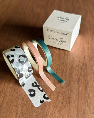 Set of washi tape with leopard print and solid colors next to a box labeled 'jane's Agenda' on a wooden surface.