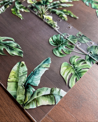 Two clear acrylic plastic discbound planner cover pieces that are front and back with green leaf patterns and palm trees on a wooden surface