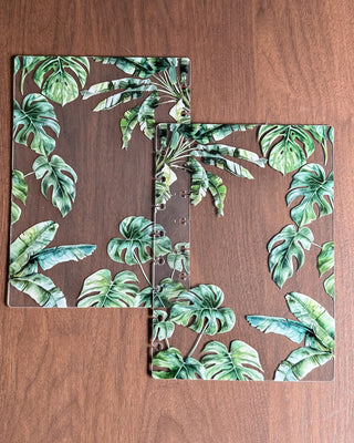 Two clear acrylic plastic discbound planner cover pieces that are front and back with green leaf patterns and palm trees on a wooden surface