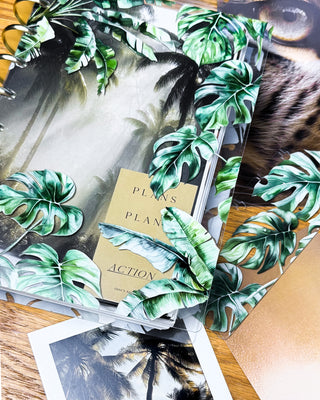 Discbound planner with tropical leaf cover design and other accessories on a wooden surface.