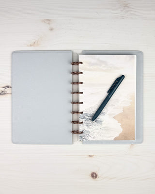 Vegan leather snap on cover on a discbound planner that is open to see the contents, as well as the inside of the cover over a light wood background.