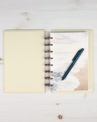 Vegan leather snap on cover on a discbound planner that is open to see the contents, as well as the inside of the cover over a light wood background.