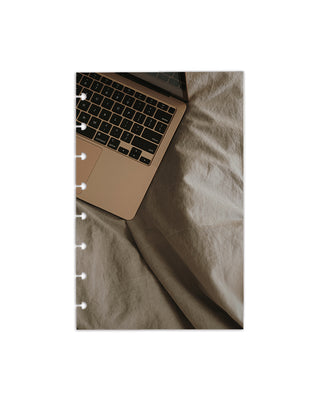 Featuring a cozy work-from-home scene with a laptop resting on a soft neutral bedspread on a white background