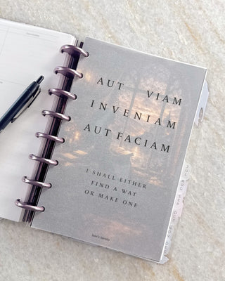 Open Jane’s Agenda discbound planner with metallic purple discs, monthly side tabs, and a frosted dashboard featuring the Latin phrase “Aut viam inveniam aut faciam” and its English translation, “I shall either find a way or make one.”
