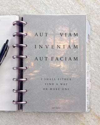 Open discbound planner with metallic discs and monthly side tabs, featuring a frosted dashboard with the Latin phrase “Aut viam inveniam aut faciam” and the English translation, “I shall either find a way or make one.”