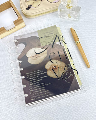 Discbound planner with clear discs and a clear cover next to other desk accessories on a gray background.