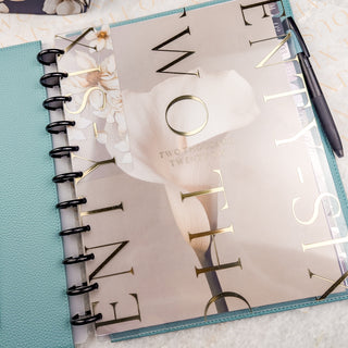 Planner cover in gold foil on clear plastic with floral design and pen on a textured surface
