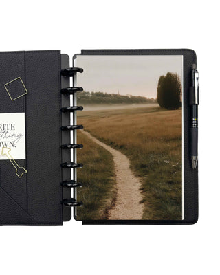 Jane's Agenda black leather discbound planner open with countryside path photo dashboard, black metal binding discs, pen loop, and interior pocket accessories