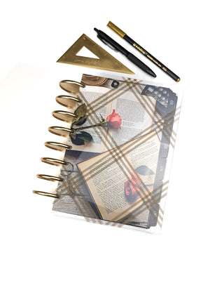Discbound planner with gold discs, pens, ruler, and decorative books and roses cardstock dashboard with a clear plaid planner cover on a white background